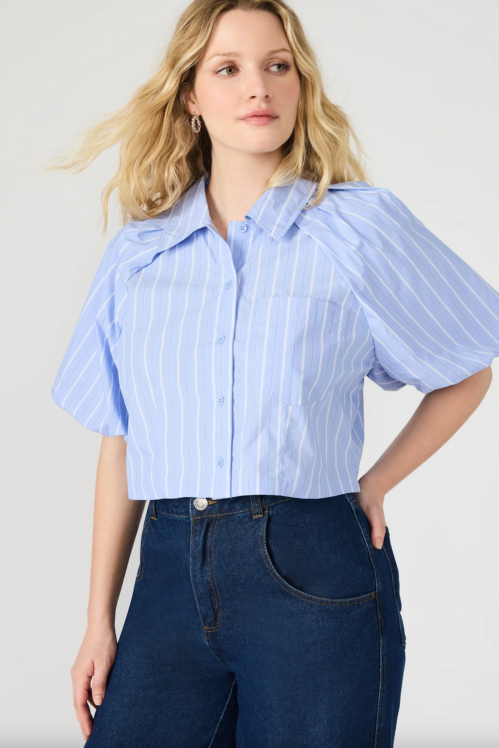 Woman wearing a light blue and white striped shirt with puffed sleeves against a plain background