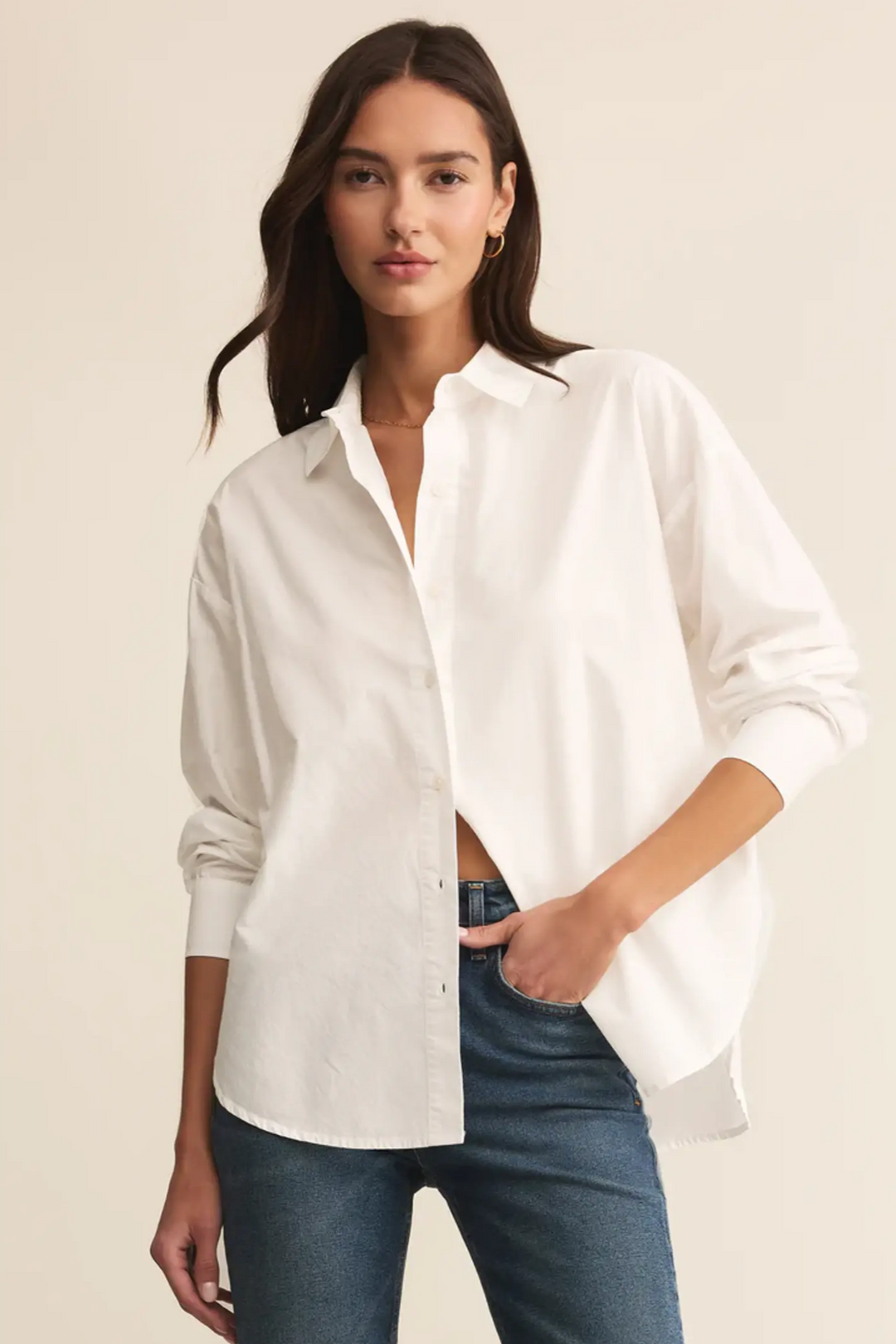 Woman wearing a white button-up shirt and blue jeans on a beige background